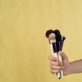 Mostre de ruj în diferite nuanțe de roșu, roz și nude aplicate pe dosul unei mâini, lângă câteva tuburi deschise