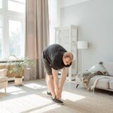 Femeie care face exerciții ușoare de întindere dimineața, pe un covoraș, într-o cameră luminoasă cu plante