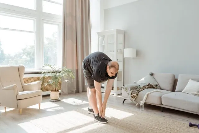 Femeie care face exerciții ușoare de întindere dimineața, pe un covoraș, într-o cameră luminoasă cu plante