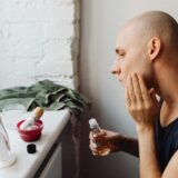 Bărbat care își aplică o cremă hidratantă pe față în fața oglinzii din baie, dimineața